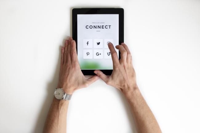 Hands holding a tablet with social media icons