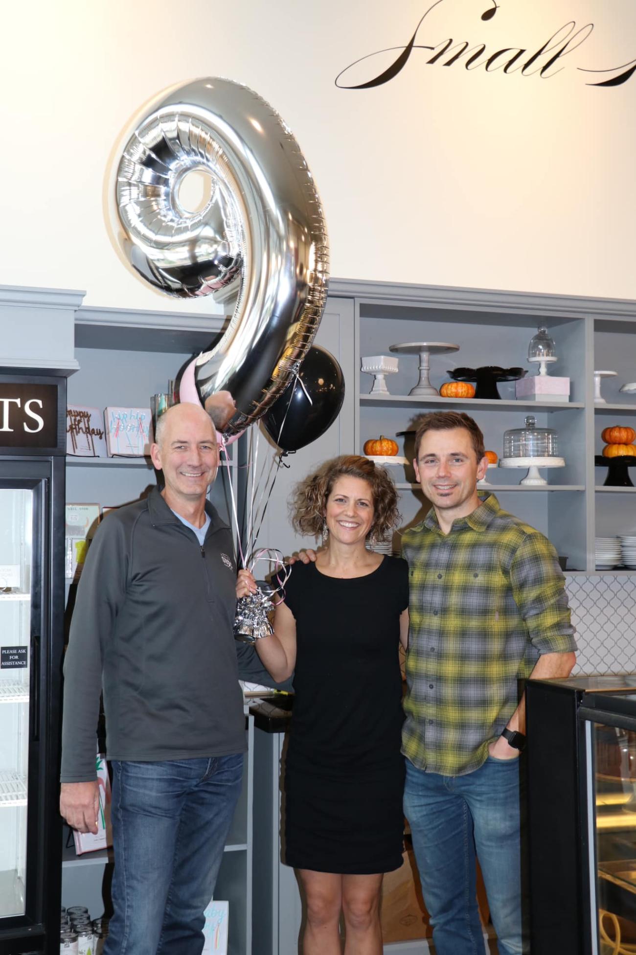 Three owners of Pure Bliss stand holding a silver helium balloon.